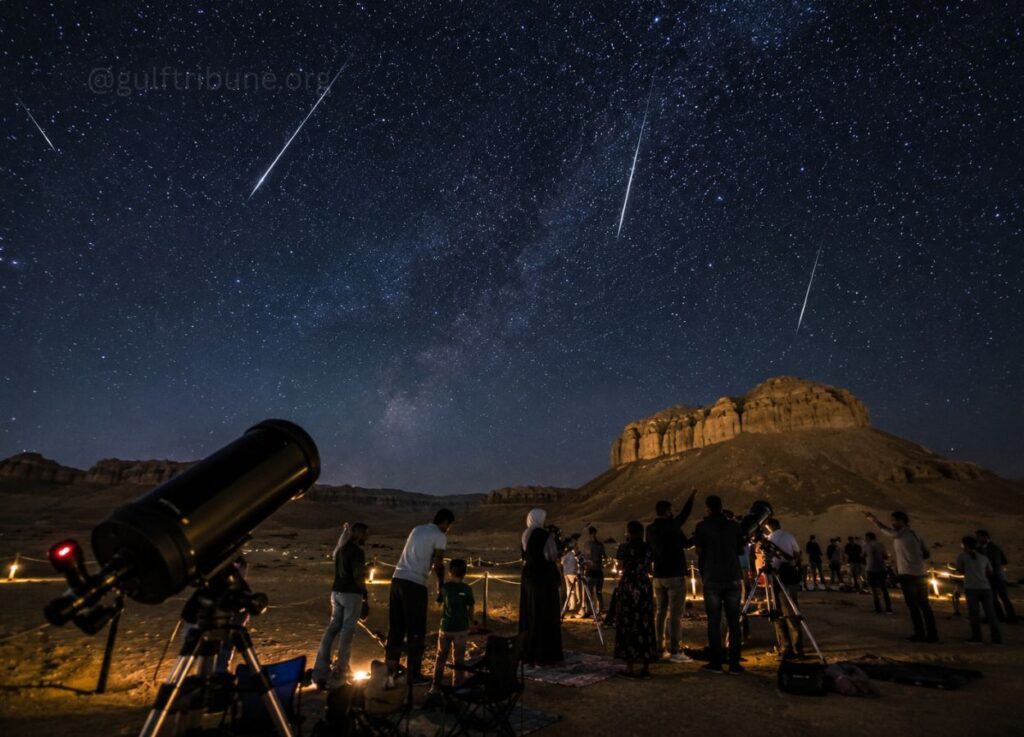 Group of people with telescopes watching a meteor shower under a star-filled night sky in a desert landscape