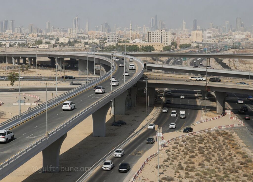 Aerial view of a complex elevated highway interchange with several overpasses and cars, city skyline in the background at distance.