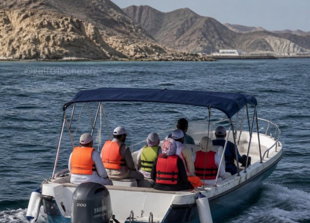 Group of people in orange and red life jackets riding a small motorboat with a blue canopy along a rocky coastline.